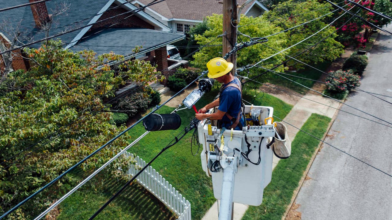services-03 Electrician in a bucket lift repairing power lines from a utility pole in a suburban neighborhood.
