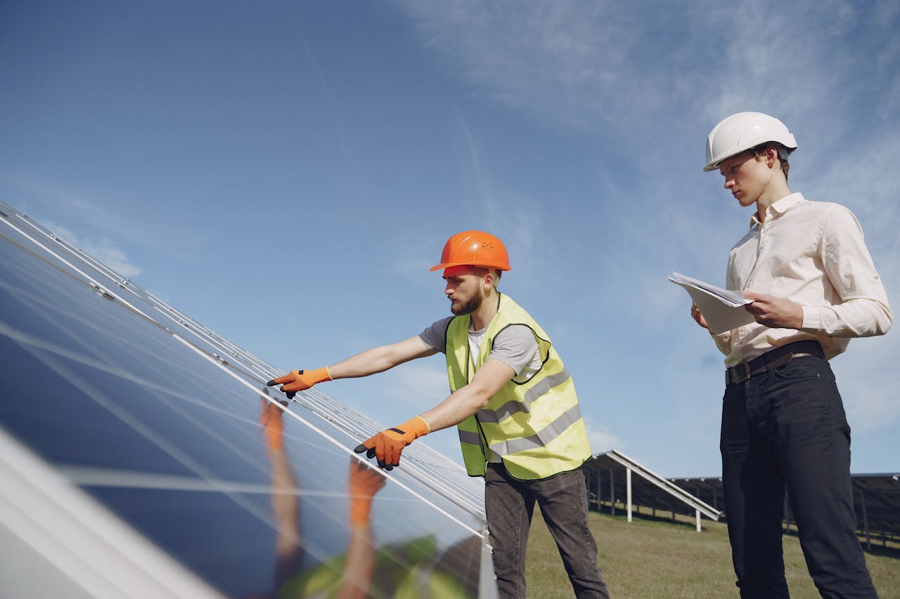 about-02 From below of bearded electrical technician in yellow vest and hardhat demonstrating solar panels to young male inspector in formal wear